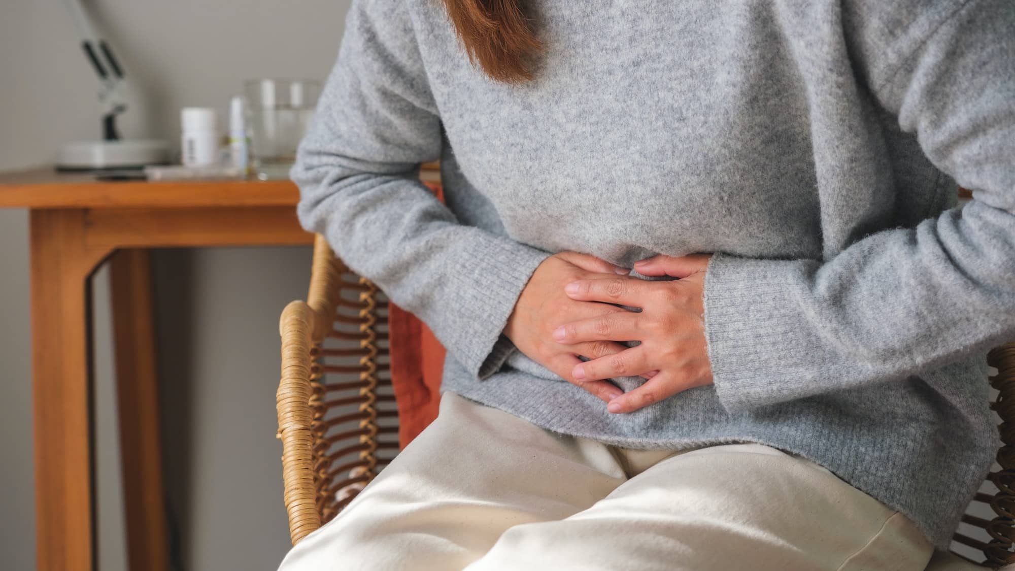 A sick woman suffering from stomachache, abdominal pain while sitting on sofa at home